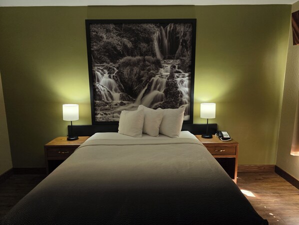 Habitación de hotel con una cama grande, dos lámparas de noche, una mesita de noche con un teléfono y un cuadro grande de una cascada en la pared.