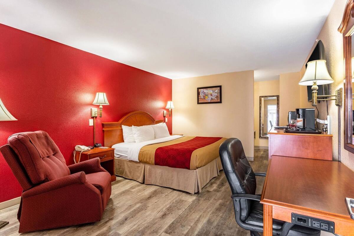 A hotel room with a bed, a desk, a chair, and a desk lamp.