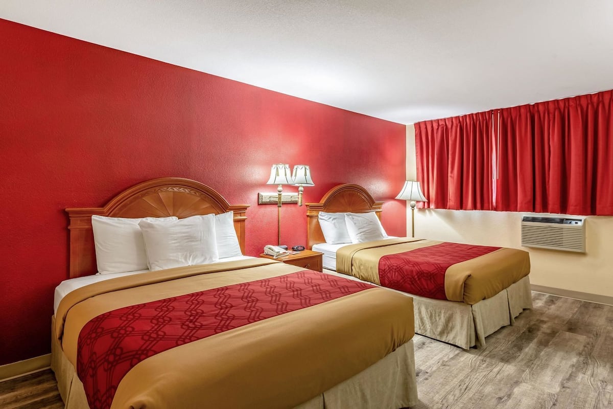 A hotel room with two beds, red walls, and a window with red curtains.