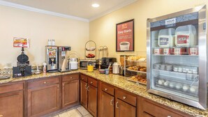A hotel kitchen with a self-service breakfast area, including a refrigerator with milk and juice, a coffee machine, and various breakfast items. - Econo Lodge Inn & Suites Santa Rosa (Santa Rosa)