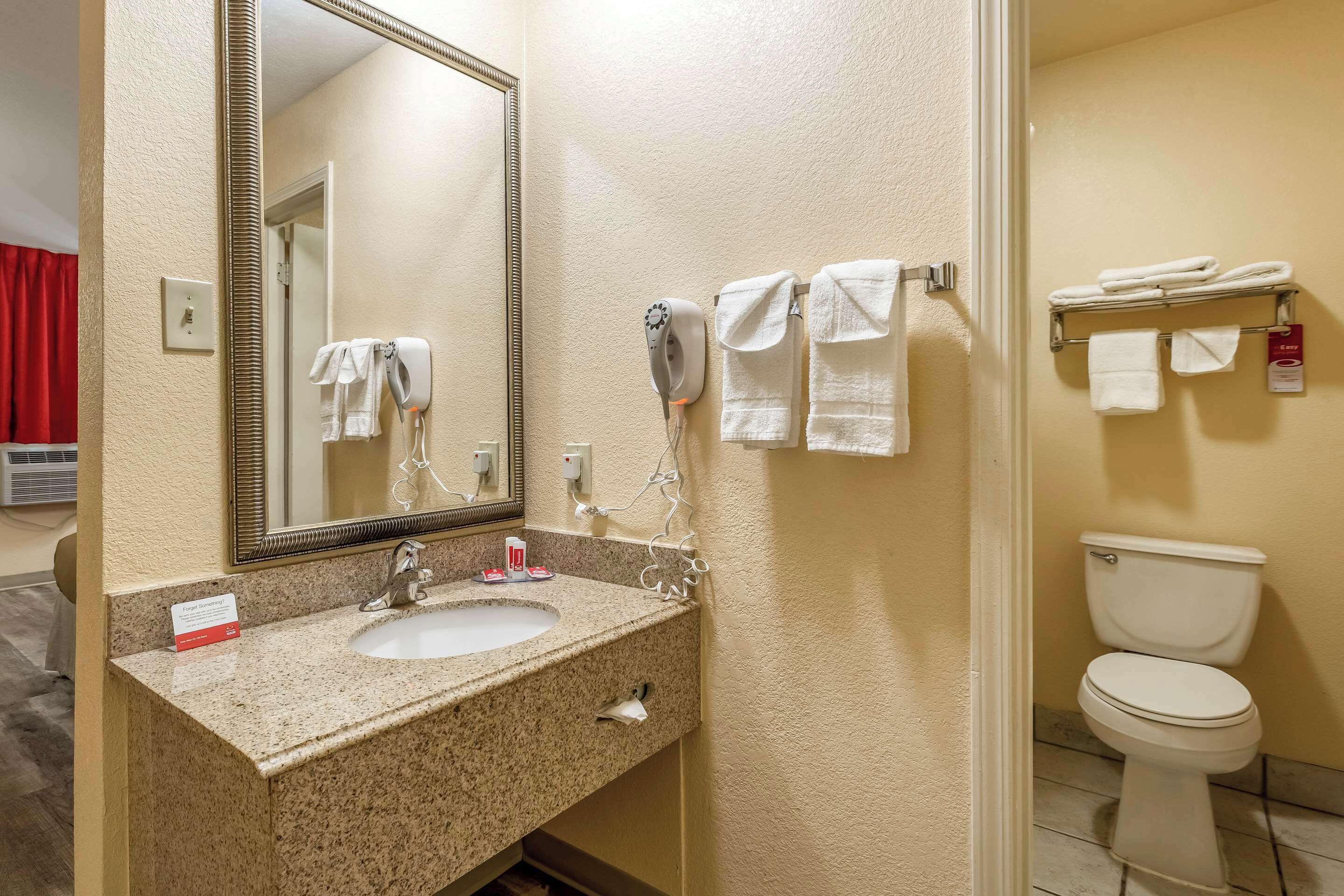 A bathroom with a granite sink, a large mirror, a hairdryer, and a toilet.