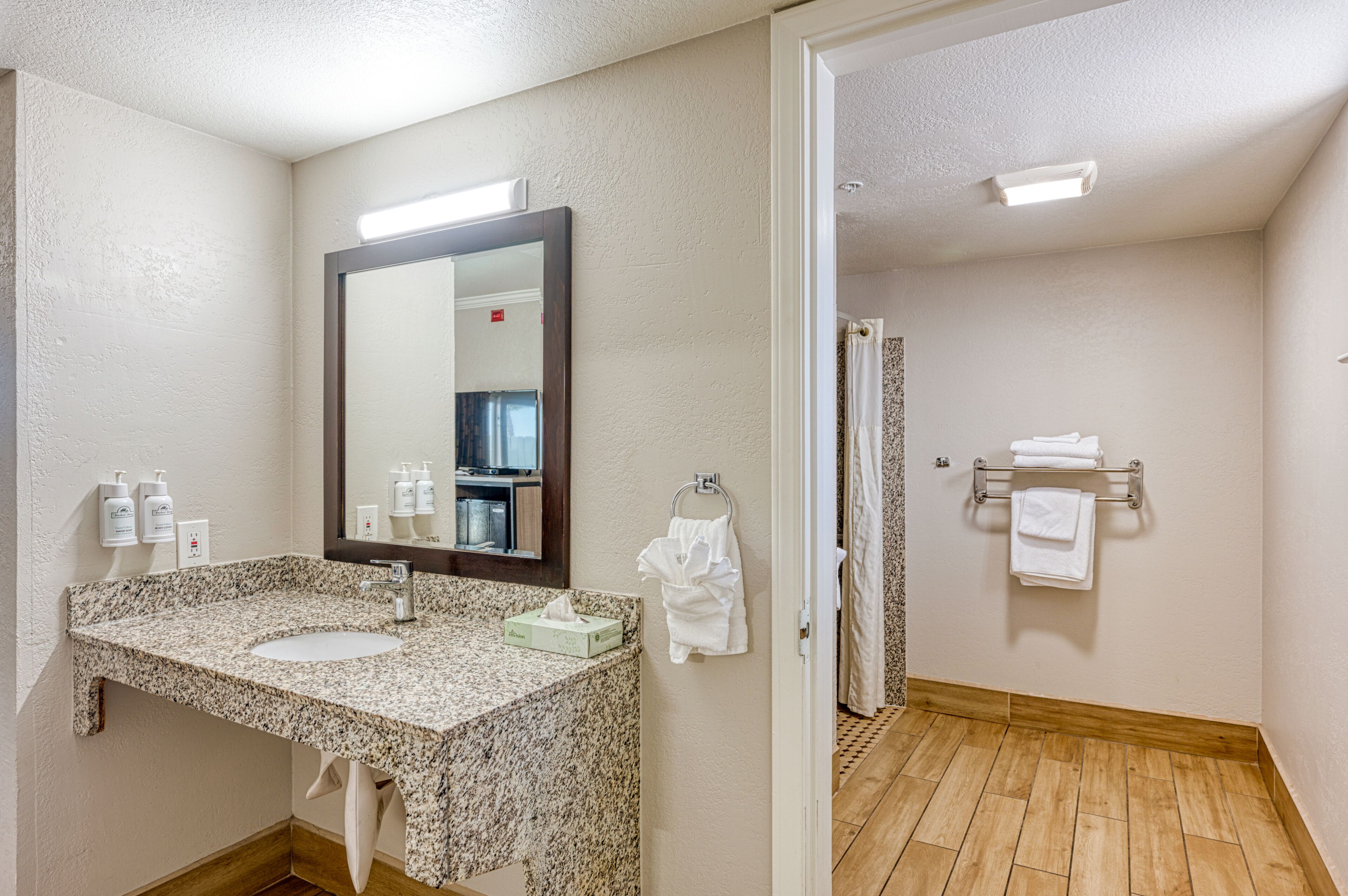 Un baño con lavabo de granito, un espejo grande, toallero y zona de ducha.