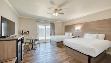Quarto de hotel com duas camas, uma escrivaninha, televisão e ventoinha no teto.