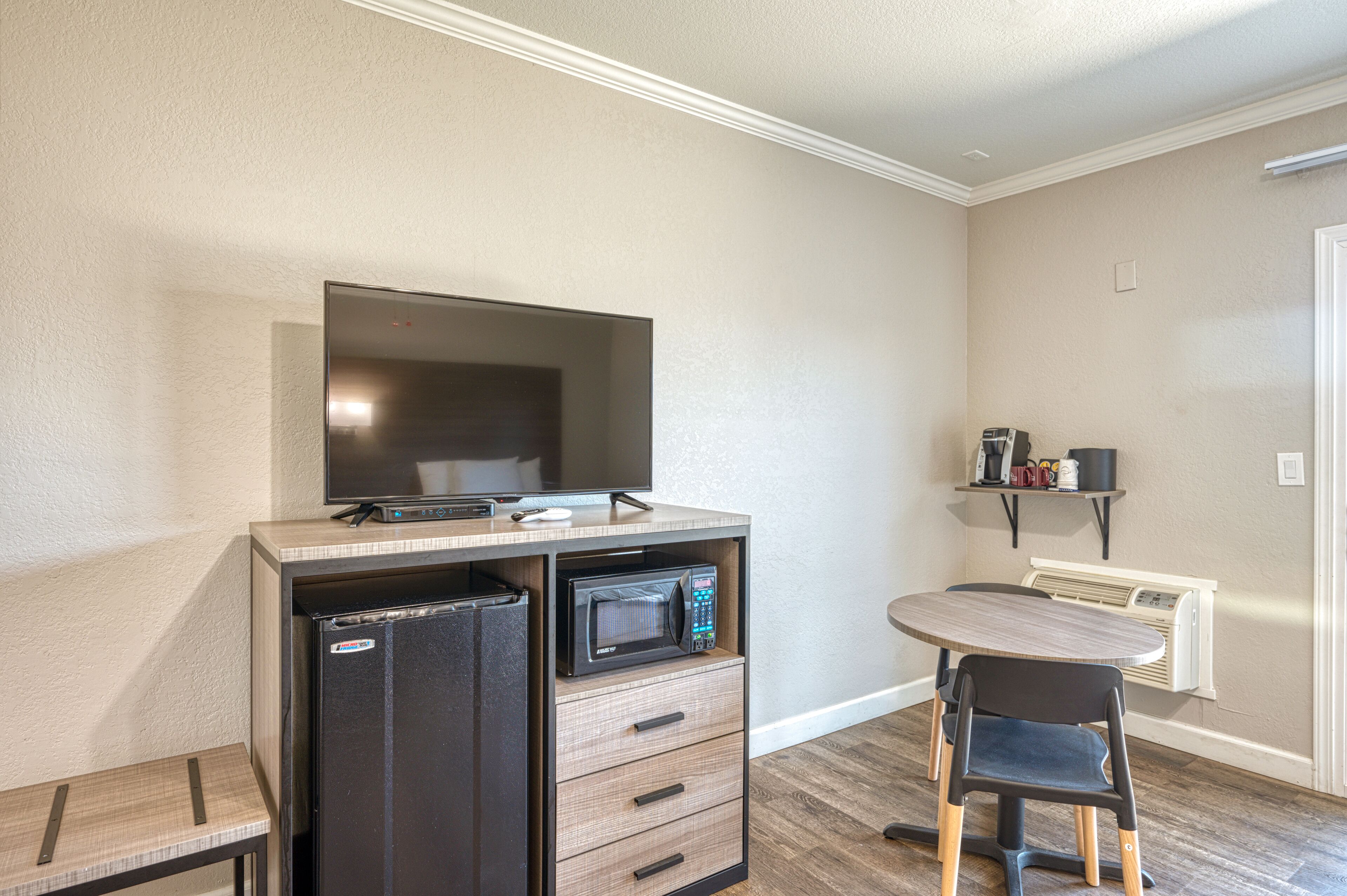 A compact kitchenette with a microwave, refrigerator, and a flat-screen TV on a wooden counter.