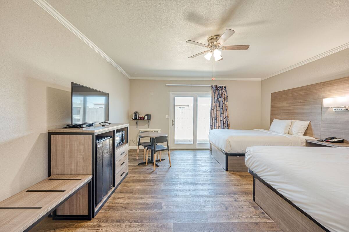 A hotel room with a desk, two beds, a ceiling fan, and a television.