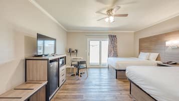 A hotel room with a desk, two beds, a ceiling fan, and a television.