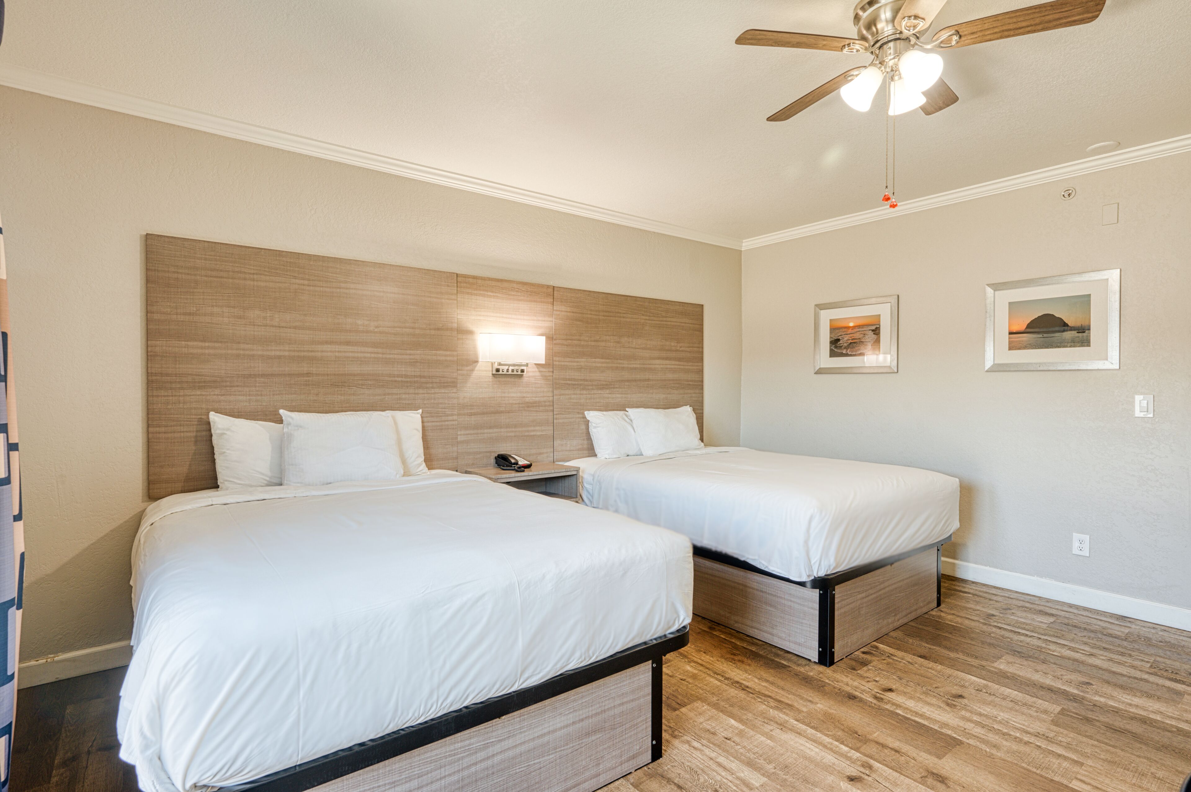 A hotel room with two beds, a ceiling fan, and wall-mounted lighting.