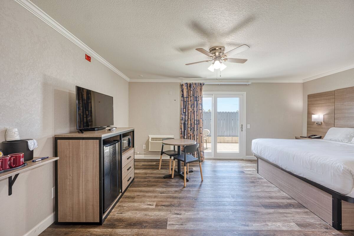 A hotel room with a bed, a desk with a TV, a chair, and a dining table.