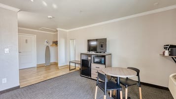 Quarto compacto com cozinha compacta, área de refeições com mesa e cadeiras, e televisão sobre um móvel.