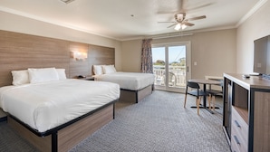 A hotel room with two beds, a desk, a chair, a ceiling fan, and a view of the outdoors. - Harbor House Inn Morro Bay (Morro Bay)
