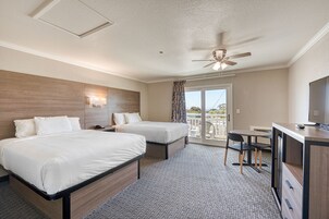 Habitación de hotel con dos camas, un escritorio, una silla, ventilador de techo y vistas al exterior.