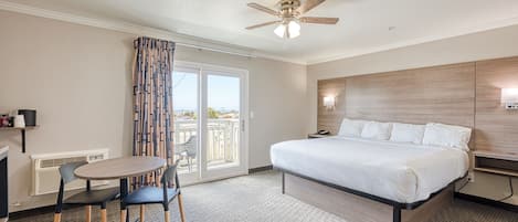 A hotel room with a bed, a ceiling fan, a table with chairs, and a view through the glass door.