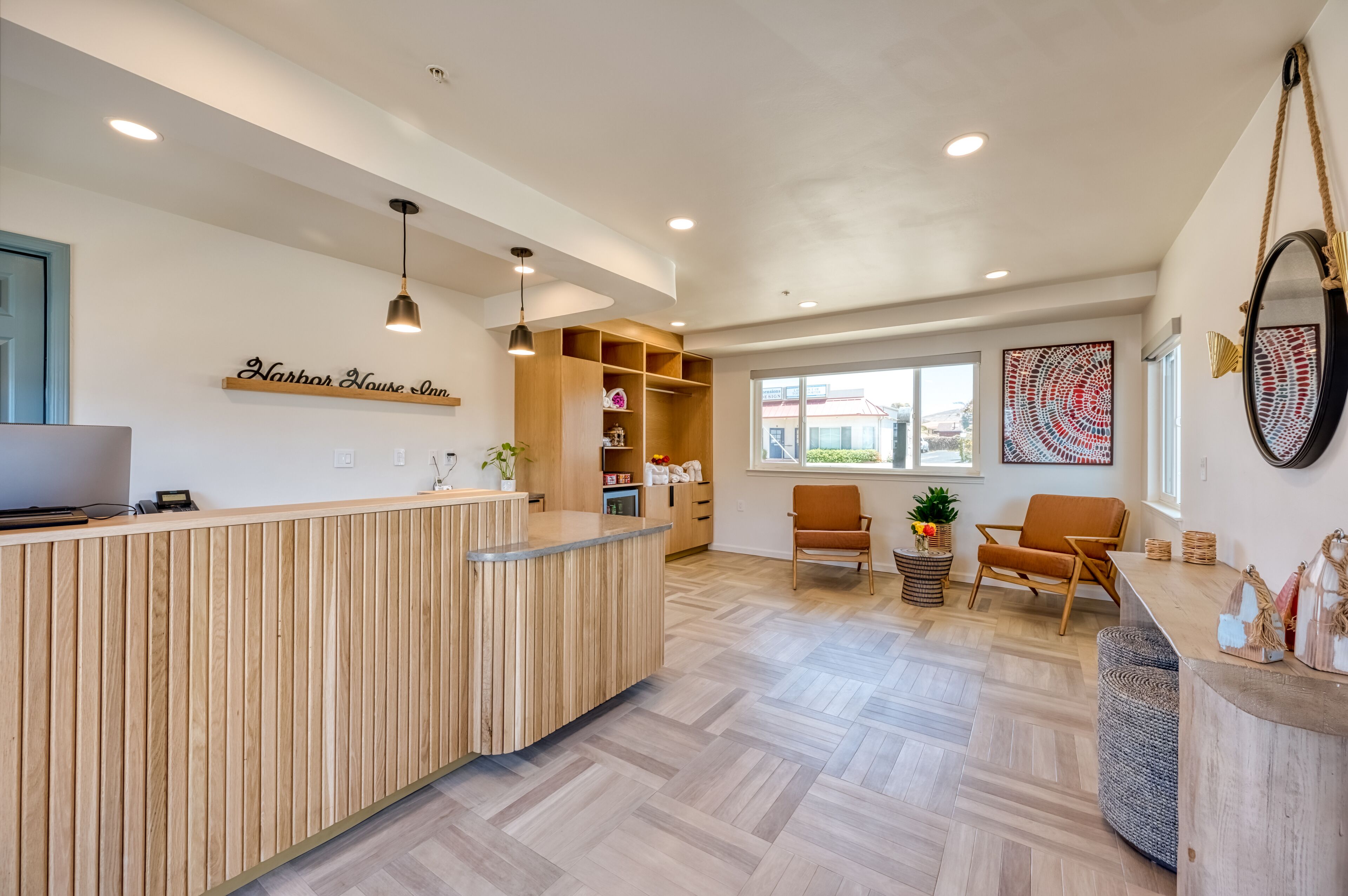 A reception area with a wooden reception desk, a seating area with two chairs, a large window with a view, and a wall-mounted mirror.