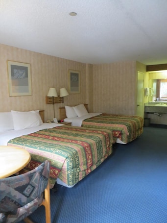 A hotel room with two beds, a desk, a chair, and a bathroom visible through an open door.