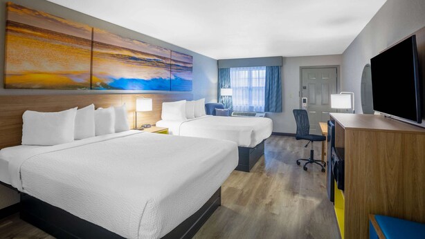 Une chambre d’hôtel avec deux lits, un bureau, une chaise, une télévision et un grand tableau au mur.