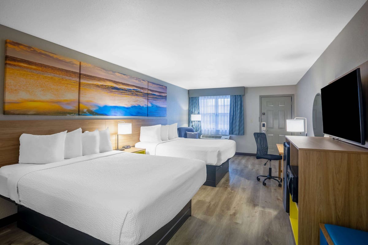 A hotel room with two beds, a desk, a chair, a TV, and a large painting on the wall.
