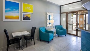 Un hall d’hôtel avec une table en marbre, des fauteuils turquoise et des tableaux encadrés accrochés au mur.