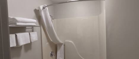 Un baño moderno con ducha envuelta en vidrio, inodoro y repisa con toallas dobladas.