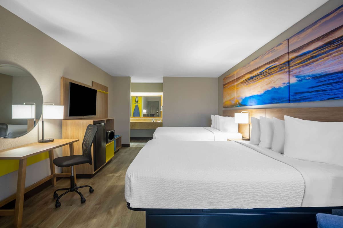 A hotel room with a large bed, a desk with a chair, a TV, and a bathroom visible through an open door.
