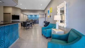 Un hall d’hôtel moderne doté d’un coin cuisine, de sièges recouverts d’un tissu turquoise et d’un miroir décoratif.