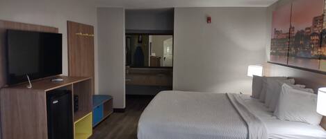 Habitación de hotel con cama, televisión, escritorio y espejo.