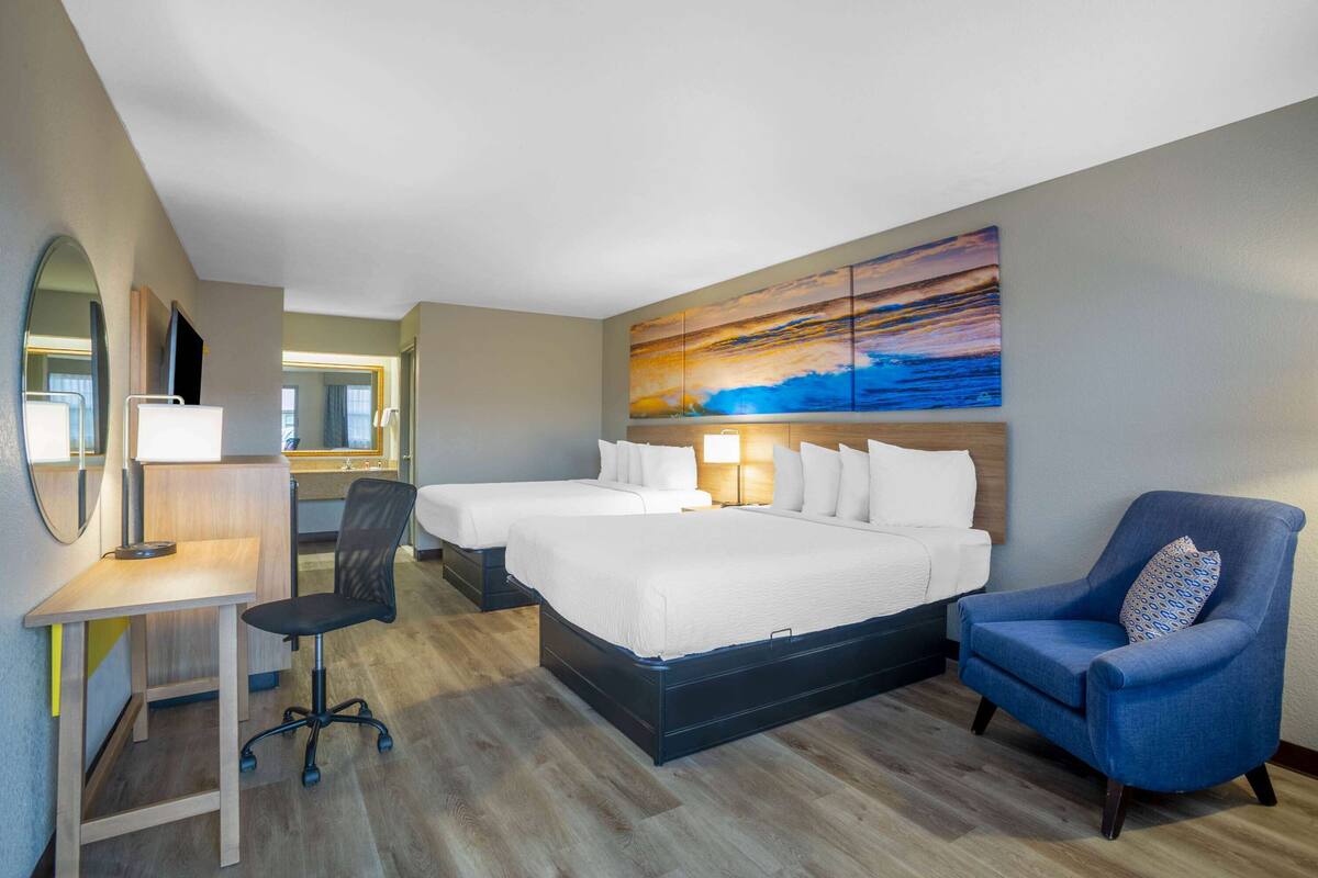 A hotel room with two beds, a desk, a chair, and a large painting on the wall.