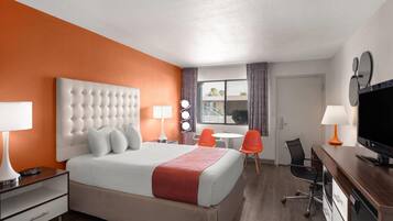 Ein Hotelzimmer mit einem großen Bett, einem Schreibtisch mit Fernseher, einem Sessel und einem Fenster mit Vorhängen.