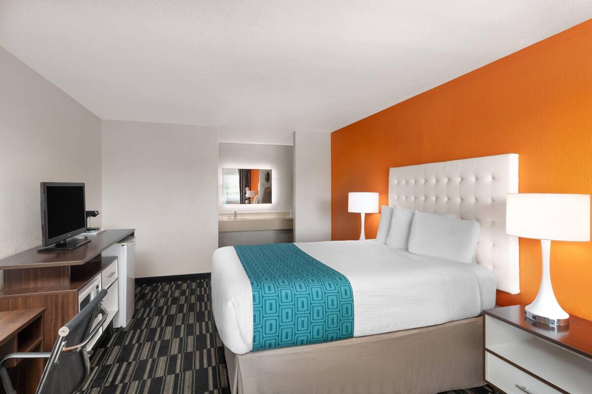 A hotel room with a bed, bedside lamps, a desk with a computer, and a mirror.