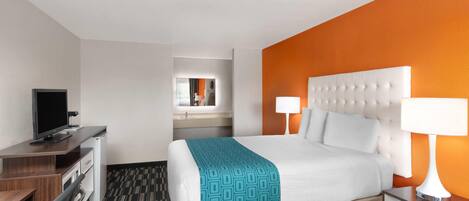 A hotel room with a bed, bedside lamps, a desk with a computer, and a mirror.