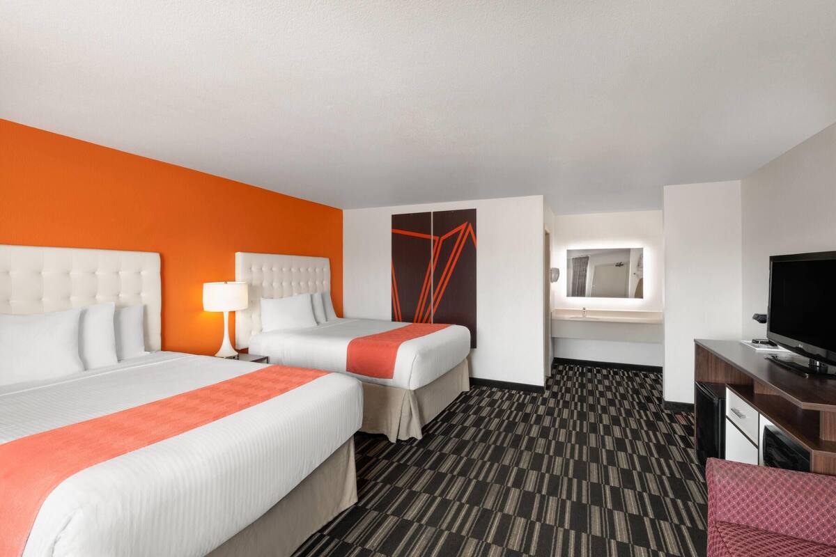 A hotel room with two beds, a desk, a TV, and a bathroom visible through an open door.