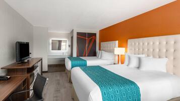 Habitación de hotel con dos camas, un escritorio con computadora, televisor y baño a la vista.