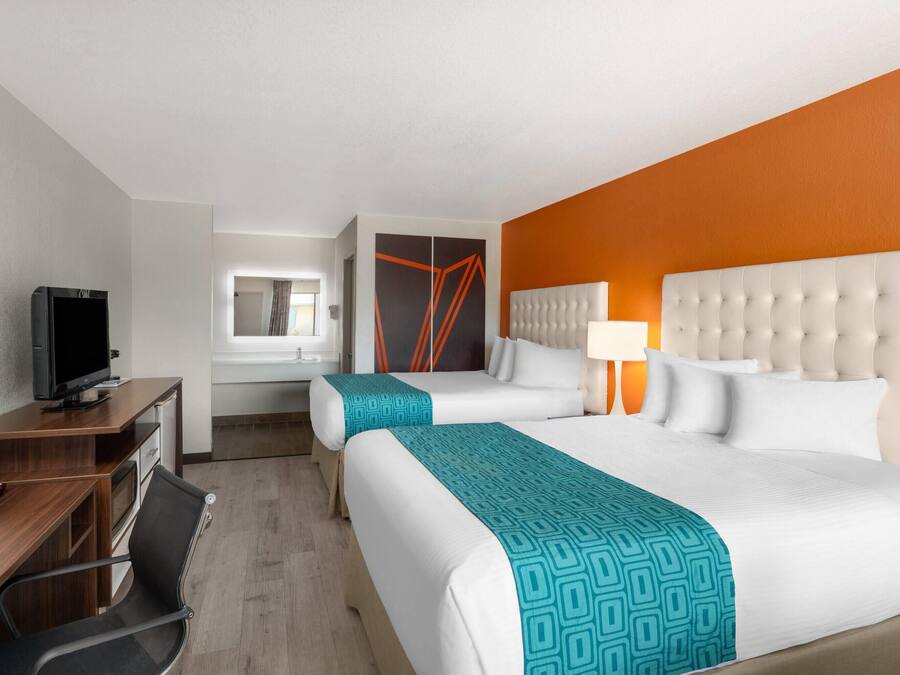 Habitación de hotel con dos camas, un escritorio con computadora, televisor y baño a la vista.