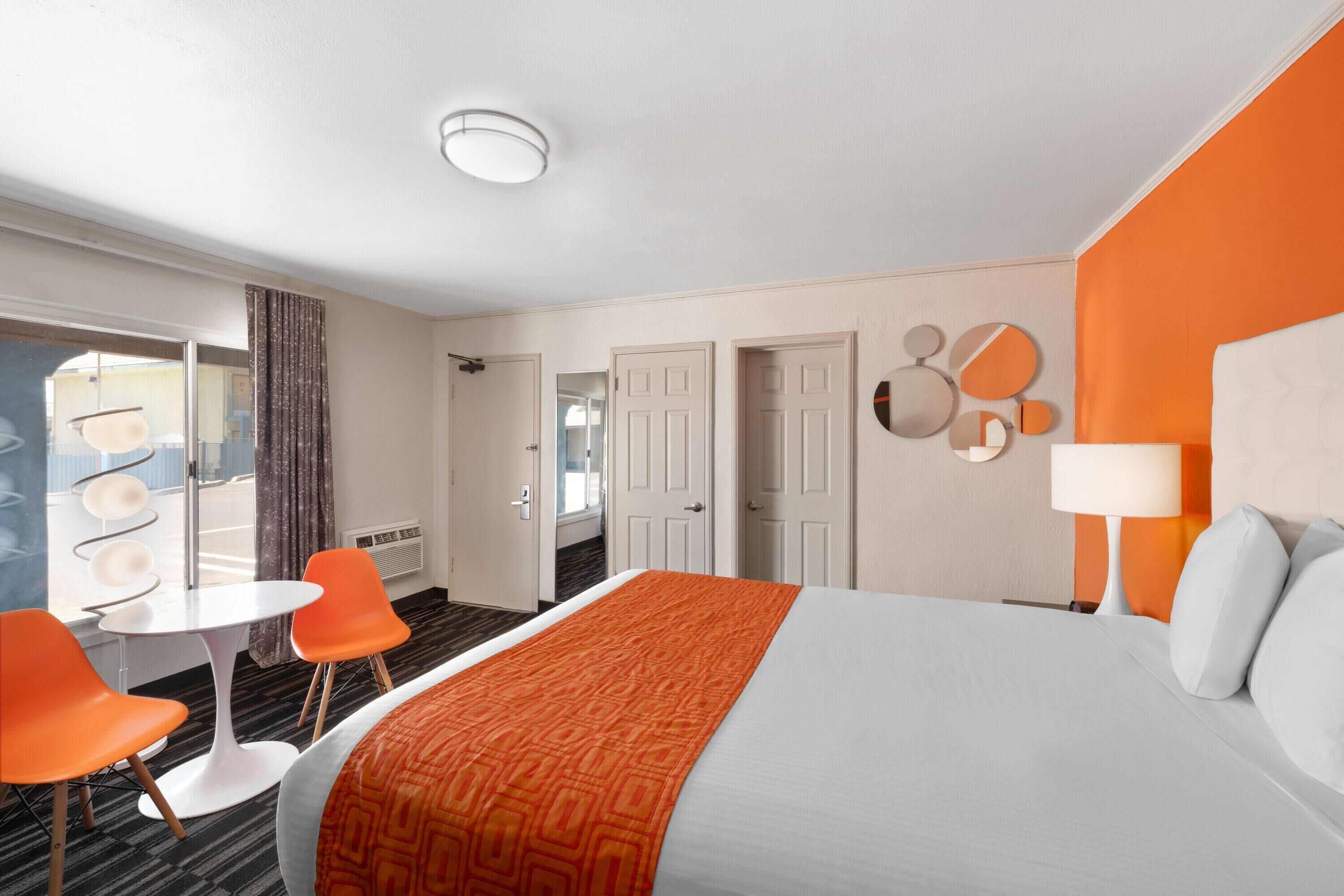Camera d'albergo con un letto grande, poltrone arancioni, un tavolino e vista all'esterno.