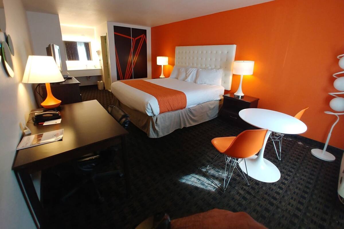 A hotel room with a bed, two bedside lamps, a desk, a chair, and a small table.