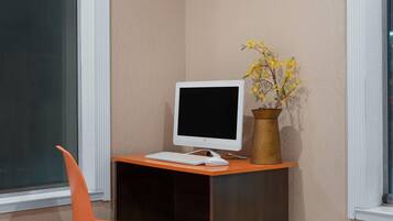 A corner desk with a computer monitor, keyboard, and a vase with yellow flowers.