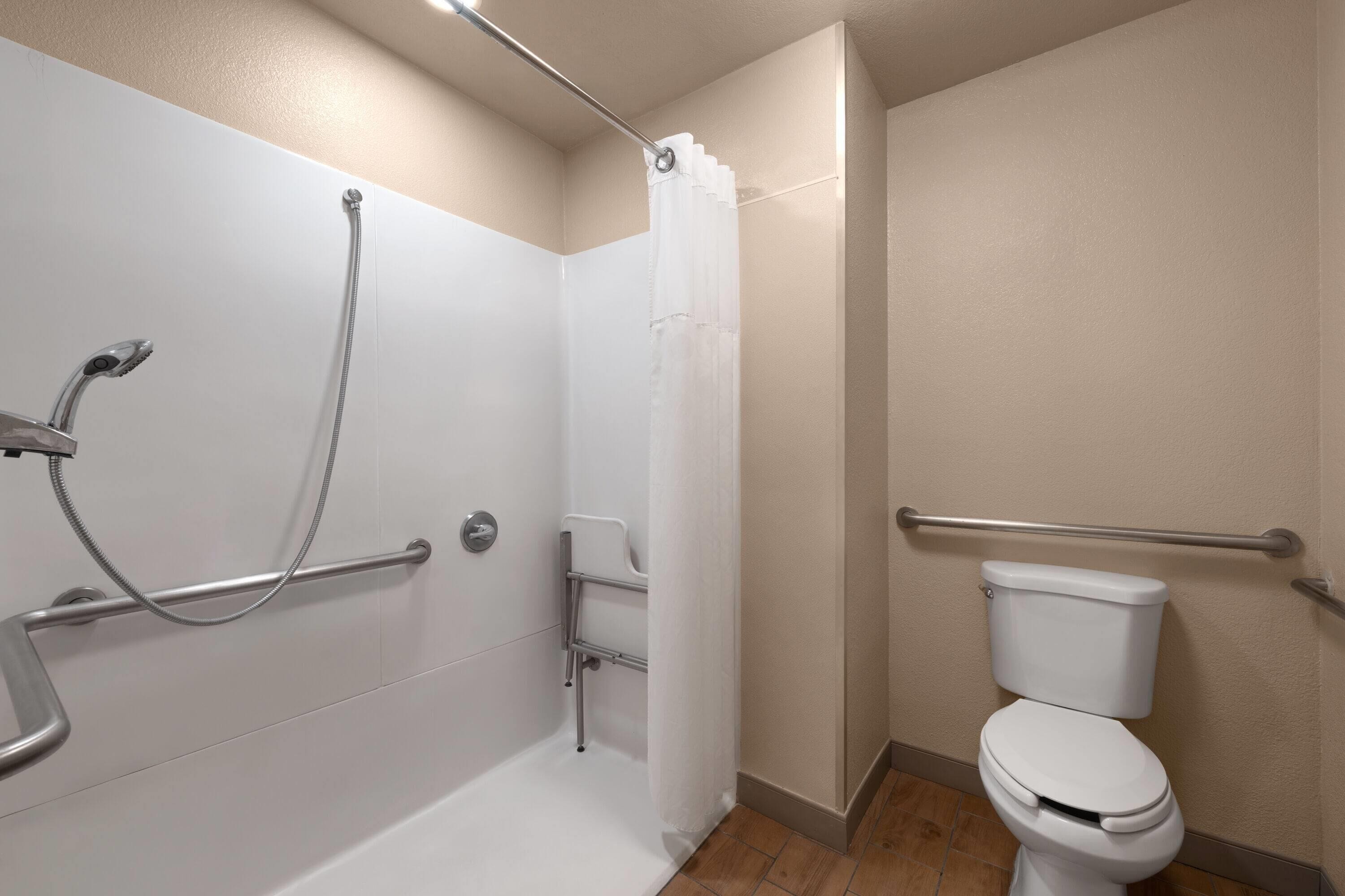 A bathroom with a shower, toilet, and grab bars.