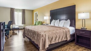 A hotel room with a large bed, a desk, a chair, and a nightstand with a lamp. - Quality Inn & Suites Canton, GA (Canton)