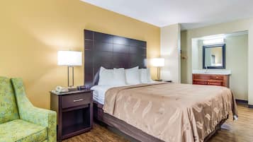 A hotel room with a large bed, bedside lamps, a nightstand, a green armchair, and a wooden floor.