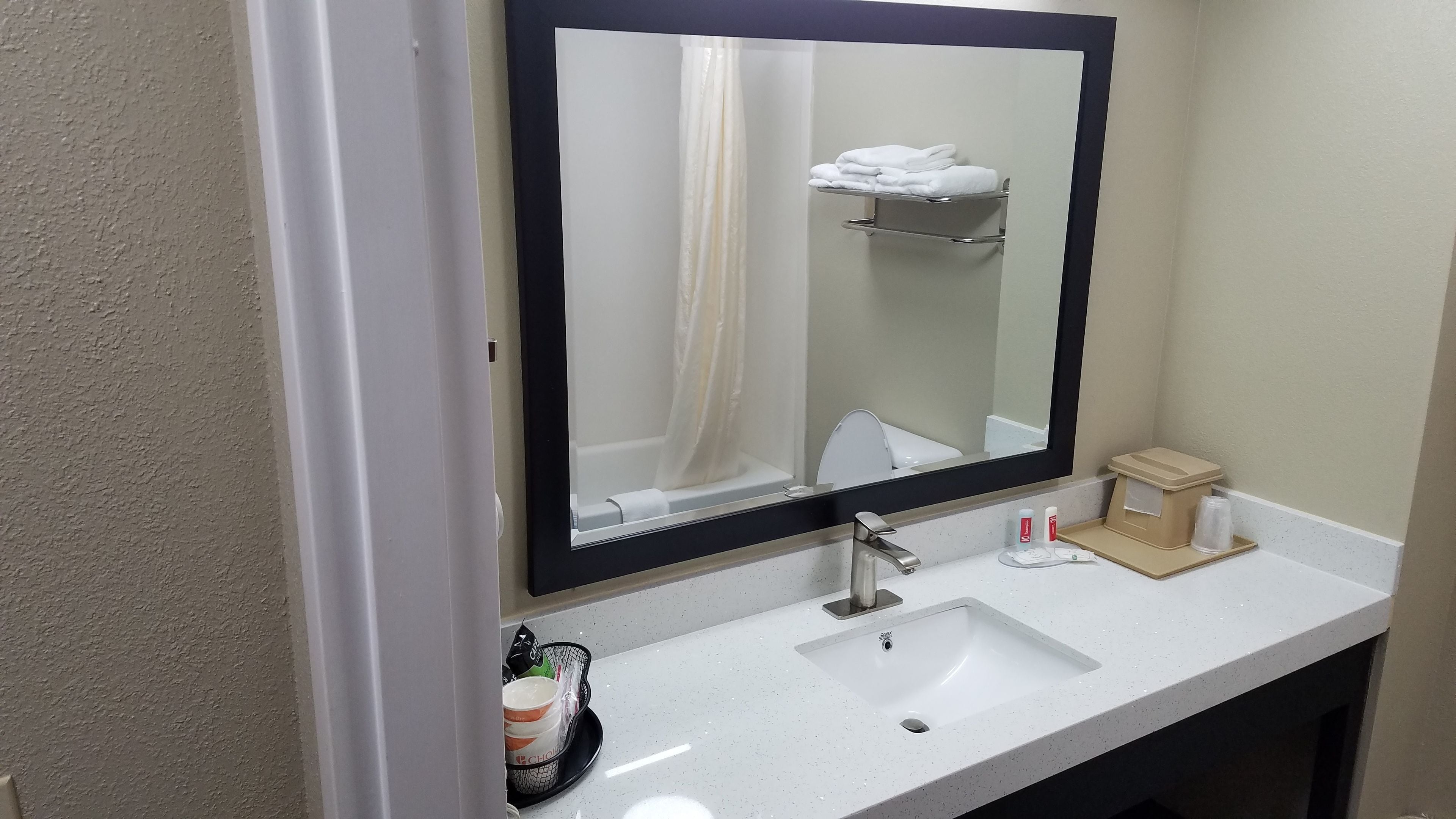 Un baño con un lavamanos blanco, un espejo, un perchero para toallas y un pequeño cubo de basura.
