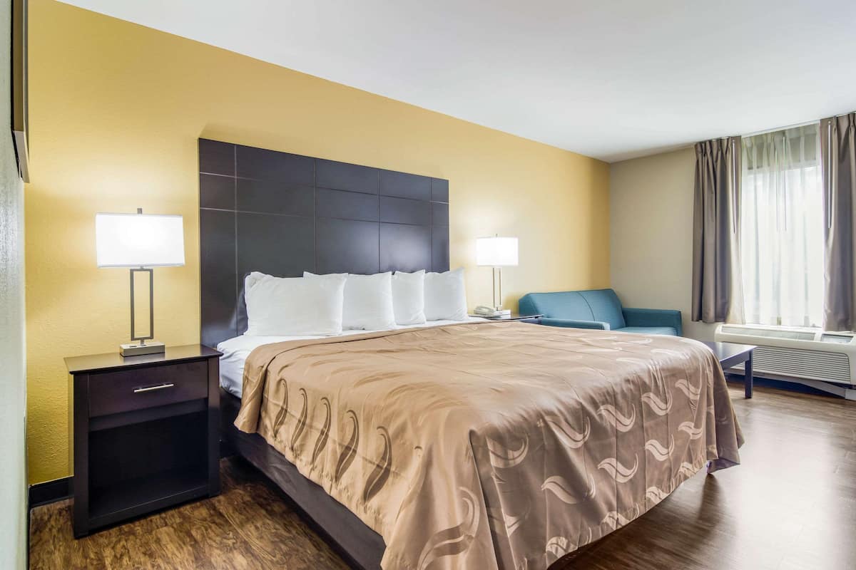 Quarto de hotel com cama, mesas de cabeceira, escrivaninha e uma cadeira.