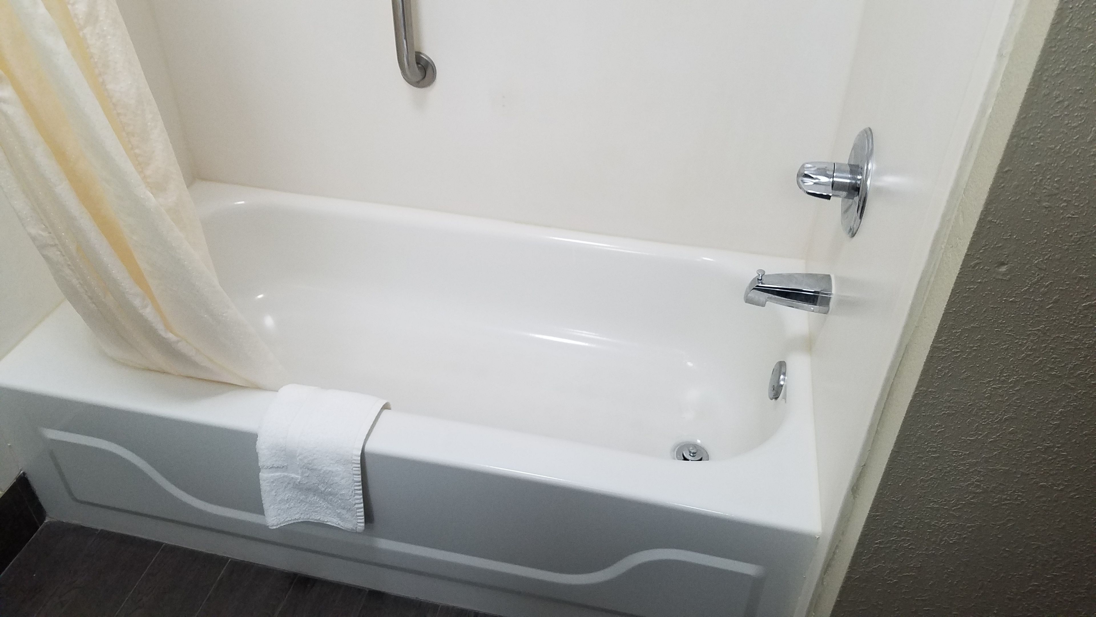 A white bathtub with a shower curtain, a towel, and a chrome faucet.