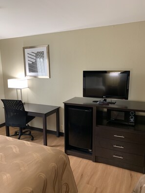 A hotel room with a bed, a desk with a chair, a television, a microwave, and a small refrigerator.