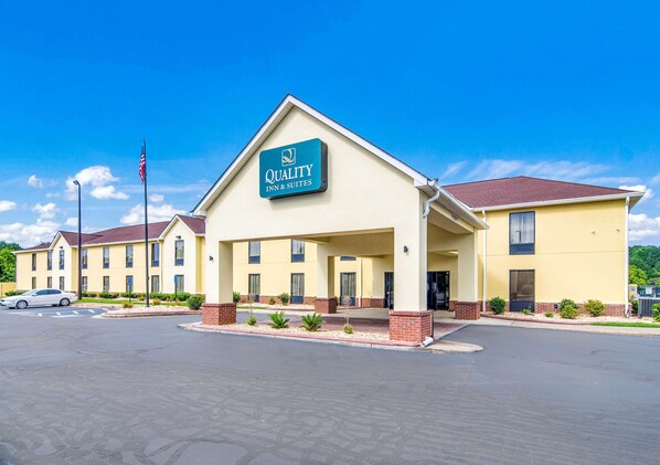 A hotel with a sign reading "Quality Inn & Suites" featuring a covered entrance, brick pillars, and a parking lot.