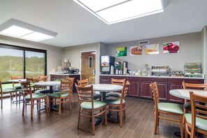 A dining area with multiple tables and chairs, a kitchen counter with appliances, and a large window offering a view of the outdoors.
