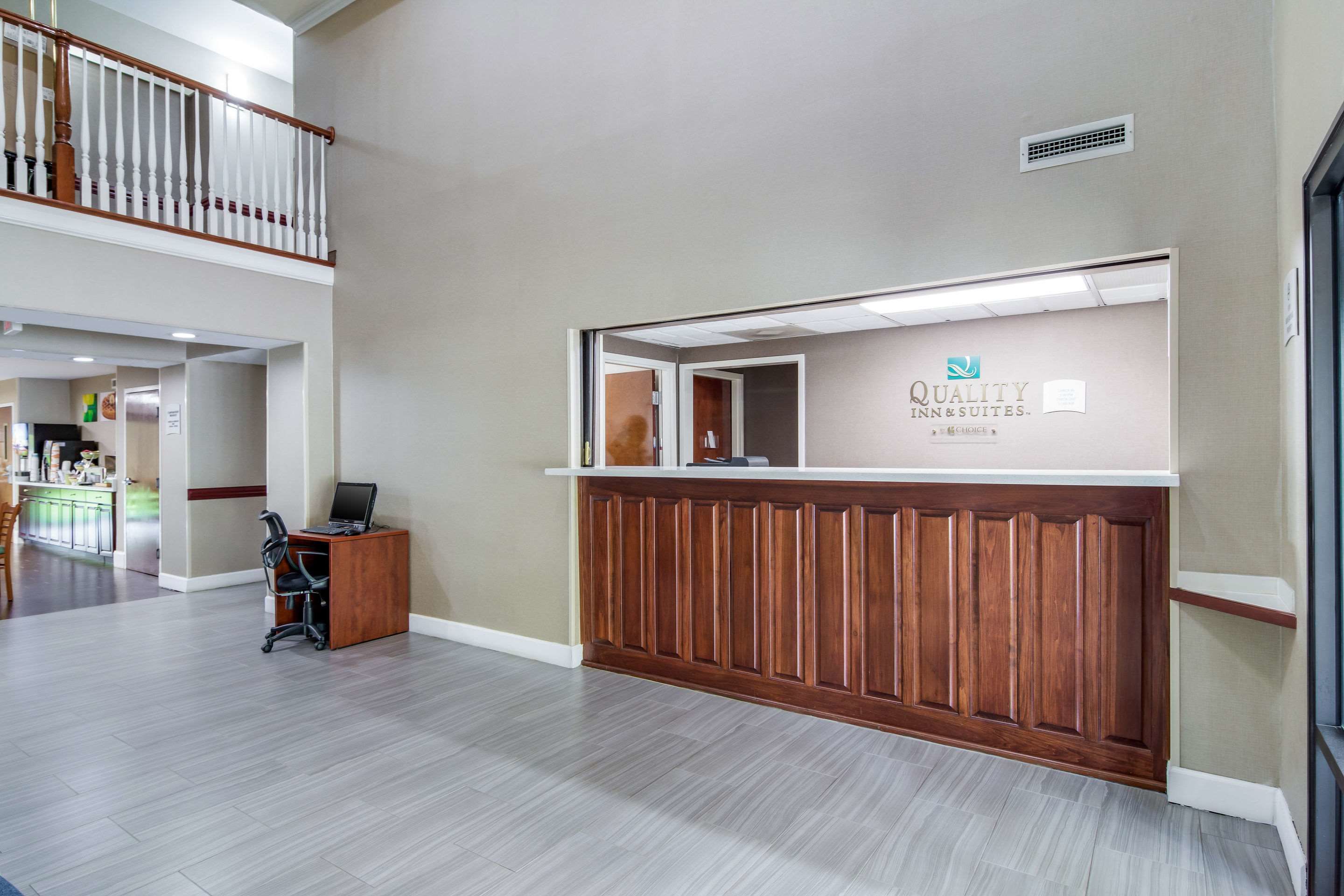 A reception area with a wooden reception desk, a computer, and a sign for Quality Inn & Suites.
