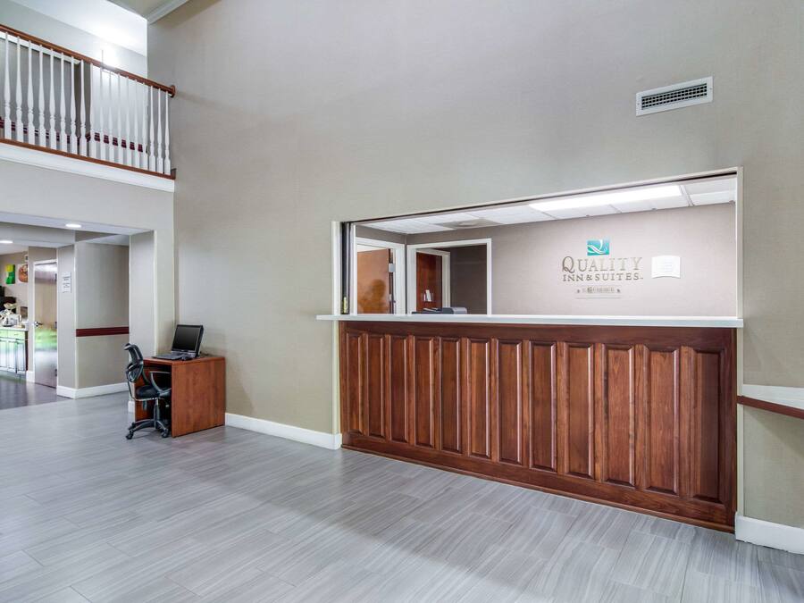 A reception area with a wooden reception desk, a computer, and a sign for Quality Inn & Suites.