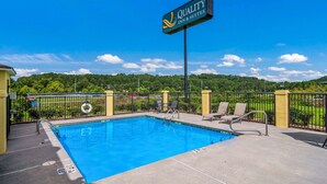A clear blue swimming pool with a sign for Quality Inn & Suites, surrounded by a fence, chairs, and a view of greenery. - Quality Inn & Suites Canton, GA (Canton)