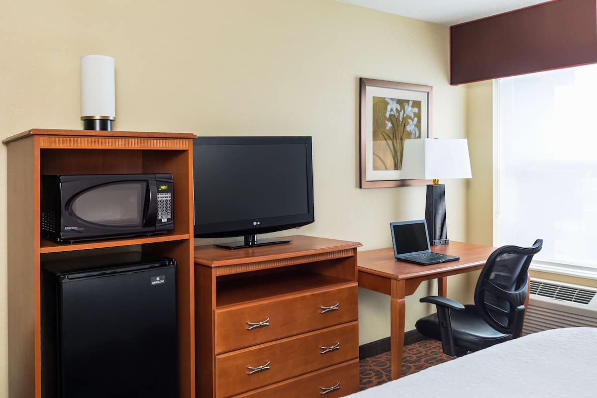 A hotel room with a bed, a desk with a computer, a television, a microwave, and a refrigerator.