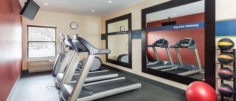 Une salle de sport équipée de tapis de course, d’un mur avec des miroirs, d’une horloge et de ballons d’exercice.