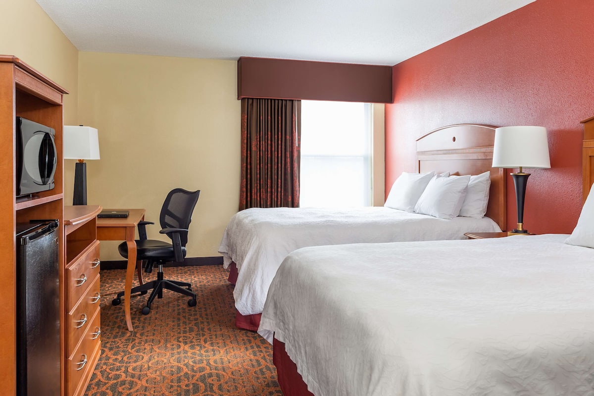 A hotel room with two beds, a desk with a chair, a television, and a wardrobe.